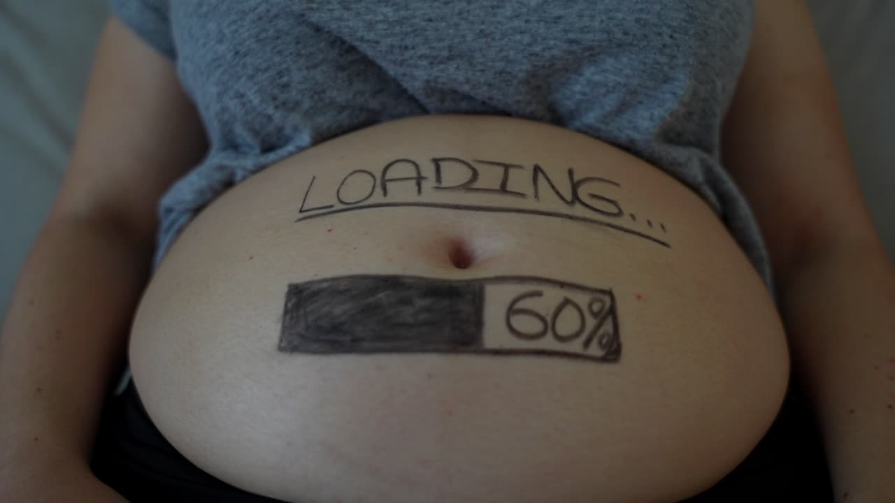 primer plano del vientre de la madre embarazada con un texto humorístico de progreso de "carga"