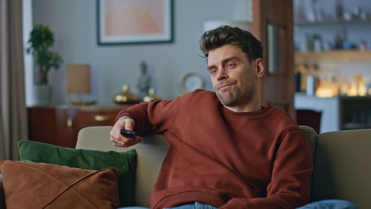 Kedsommelig hipster vælger film og slapper af på sofaen tæt på. Mand skifter kanaler.