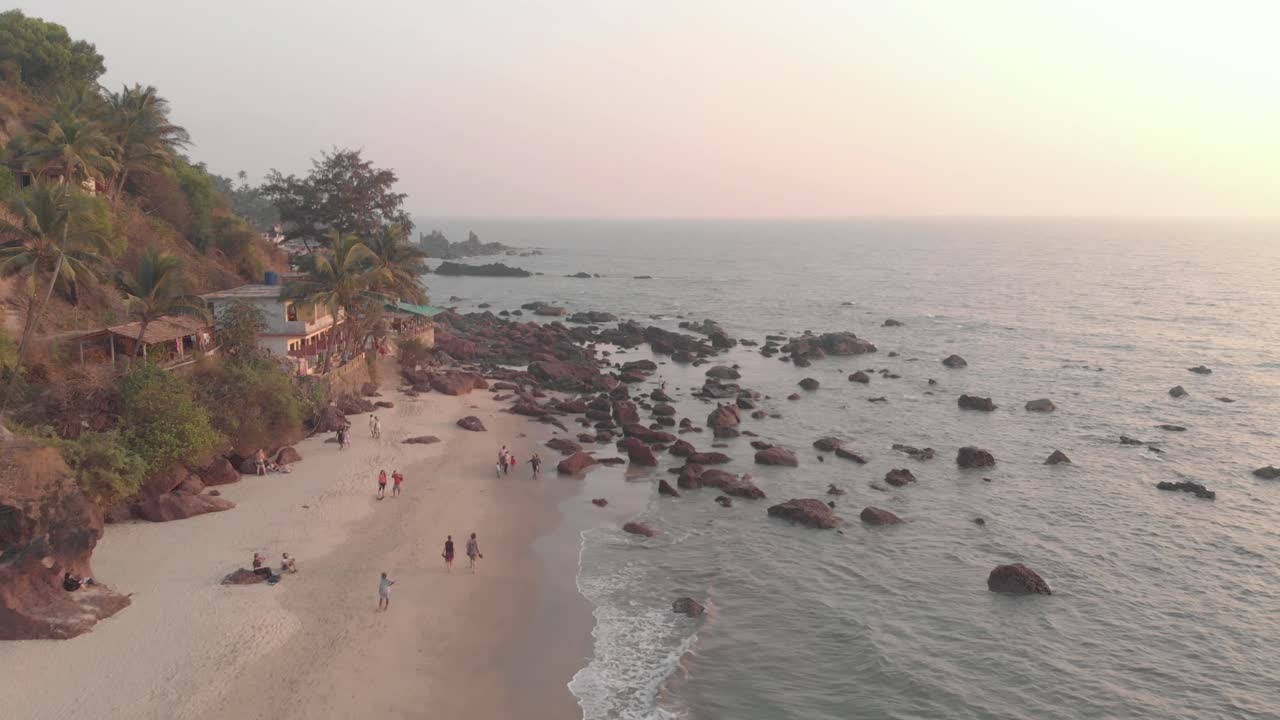 People walking on Arambol sand beach, palm trees and calm waters. Goa, India.
