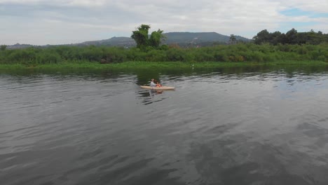 Aerial-shot-orbiting-around-a-man-with-a-life-jacket-in-a-kayak-paddling-along-swamp-near-Lake-Victoria