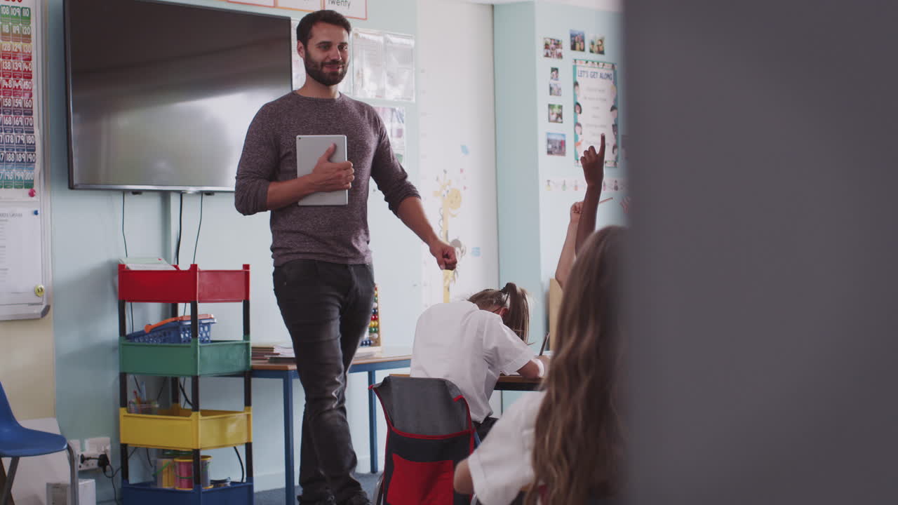 maestro masculino con tableta digital enseña a un grupo de alumnos de primaria uniformados en el aula de la escuela
