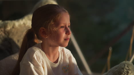 dreamy kid smiles peacefully. calm girl finds comfort in tranquil moment sitting near sunlit window in tent. cheerful kid at home in evening