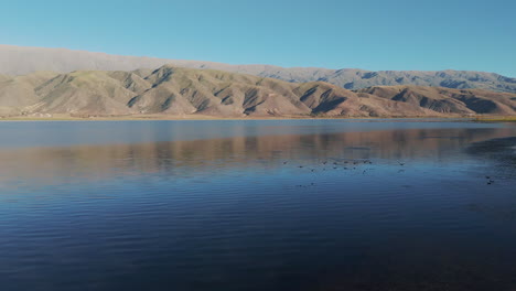 At-dawn,-birds-fly-low-over-the-La-Angostura-dam-in-Tafí-del-Valle,-Tucumán,-Argentina