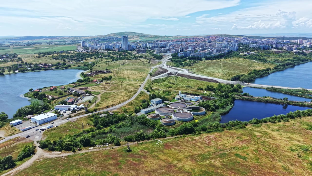Vista di una città vicino all'acqua e ai campi durante il giorno, con edifici in lontananza e strade che collegano varie aree