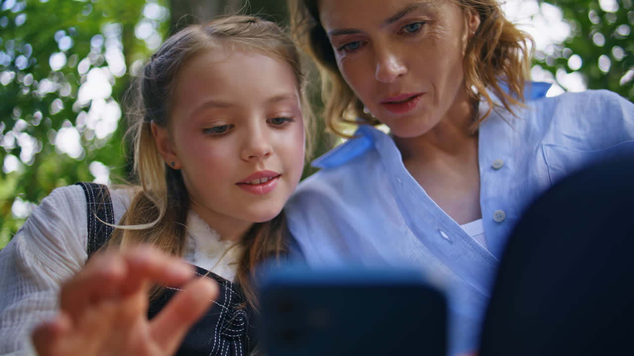 Closeup kid touching smartphone at summer greenery sitting bench with mother