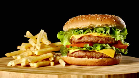 hamburguesa de carne artesanal y papas fritas en una mesa de madera aislada sobre un fondo negro.