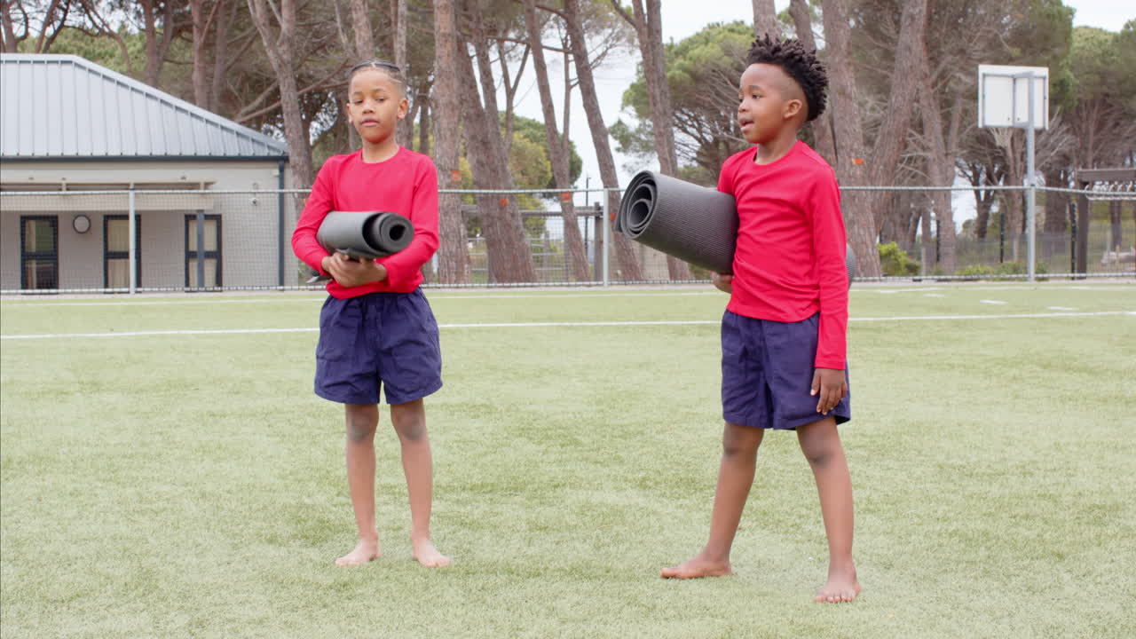 Multiracial boys playing with yoga mats on school field, enjoying outdoor activity