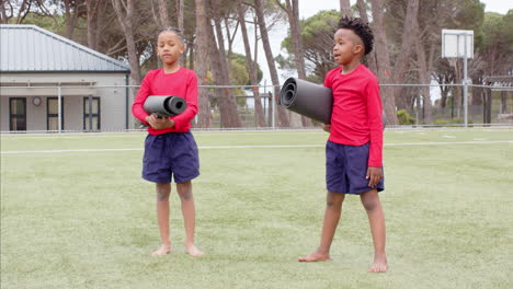 multiracial boys playing with yoga mats on school field, enjoying outdoor activity