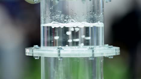 Wasserstoffgas-Sprudelt-Durch-Eine-Membran-In-Einem-Mit-Wasser-Gefüllten-Plastikzylinder,-Kleine-Blasen-Bilden-Sich-In-Der-Flüssigkeit,-Zeitlupe,-Herauszoomen