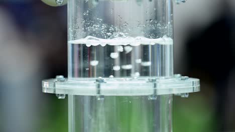 hydrogen gas bubbeling through a membrane in a plastic cylinder filled with water, small bubbles forming in liquid, slow motion, zoom out