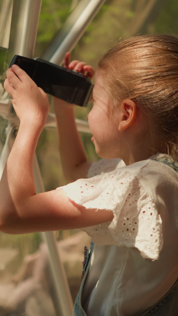 niño mira en la lente de la cámara en la cabina de glamping. niña pequeña graba video a través de la pared de vidrio en un soleado día de verano. niño toma una vista de eco camping