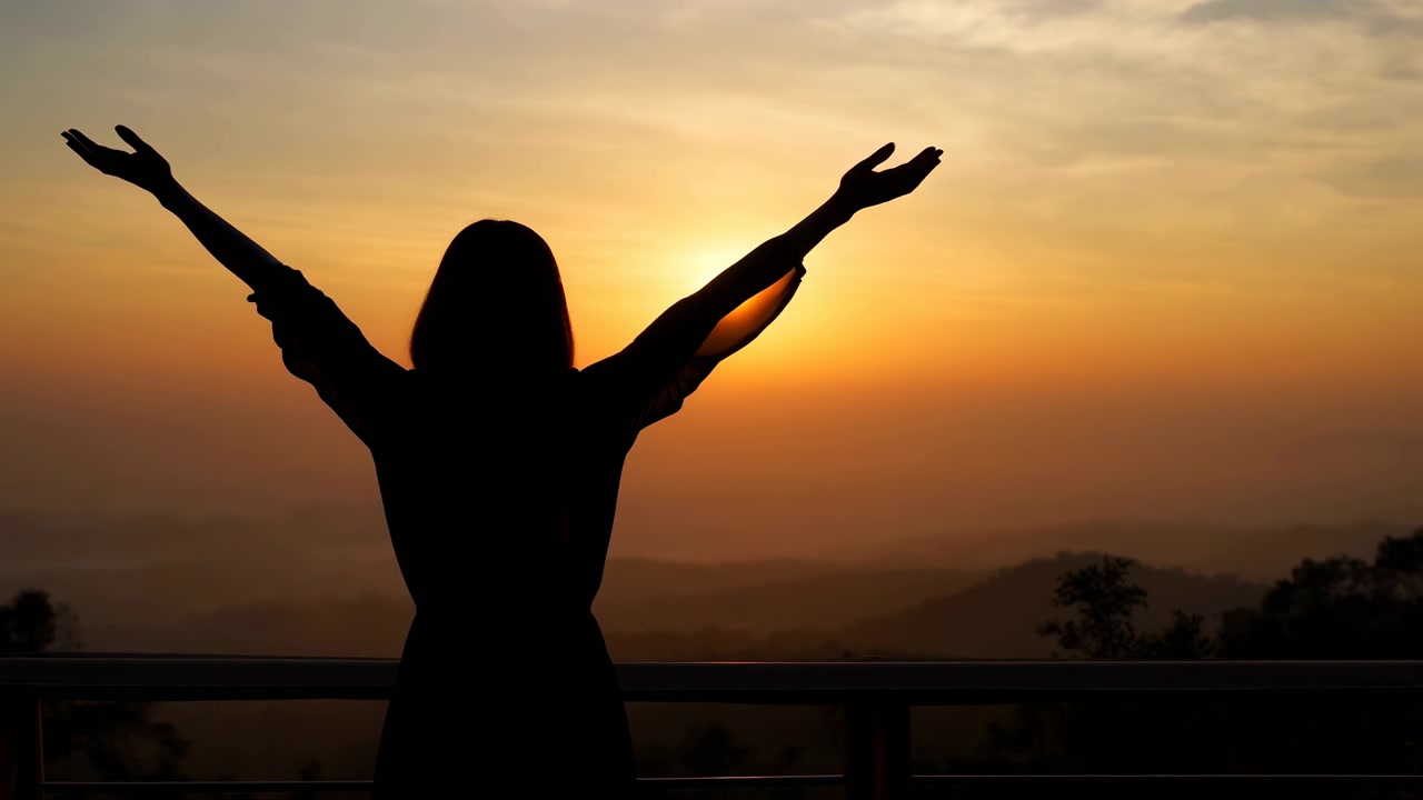 Silhouette di una persona su un balcone, braccia tese verso l'orizzonte luminoso al tramonto, con cielo caldo, nuvole leggere e paesaggio distante che creano un'atmosfera esterna pacifica, con silhouette, tramonto.