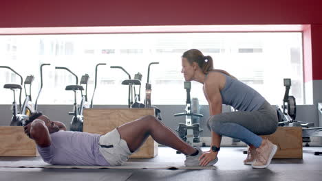 una joven blanca en forma ayuda a un hombre afroamericano durante un entrenamiento en el gimnasio.