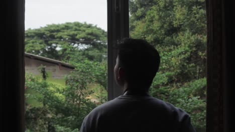 Medium-close-up-shot-of-silhouette-of-a-photographer-taking-photos-of-something-outside-the-window,-with-trees-on-the-background