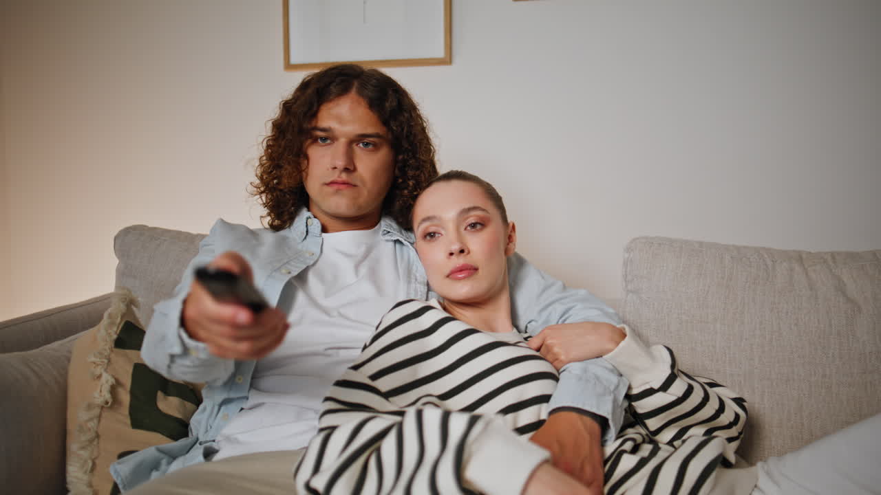 Chilling couple switching channels with remote controller at home sofa closeup