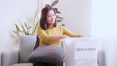 young asian woman selecting clothes for donation and making reservations for delivery and pay by credit card online