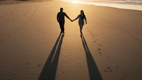 a couple strolling hand in hand on a serene beach at sunset, their shadows stretching across the warm sand beneath the glowing horizon