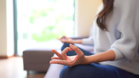 manos cercanas de una mujer bastante en forma practicando yoga sentada en un sofá en posición de loto meditando