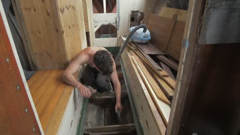 young man hoovering bilge of wooden boat interior