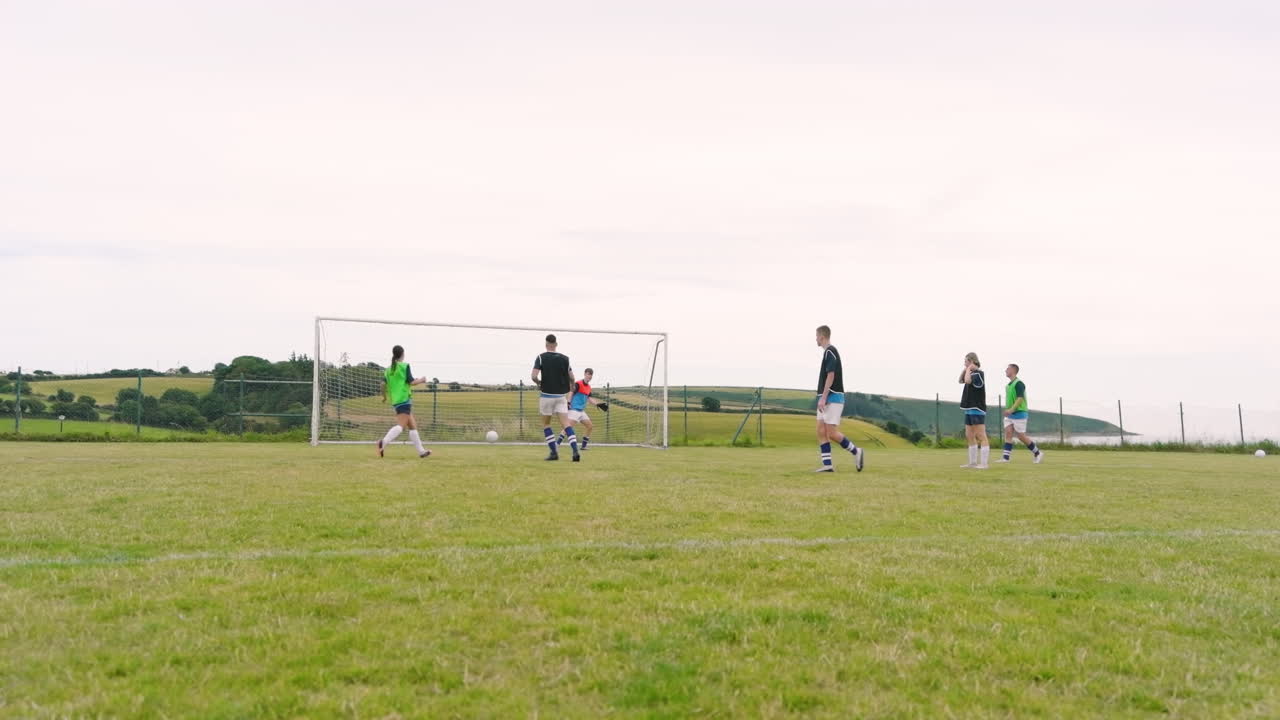 Male and female soccer players passing and shooting at goal on pitch, slow motion, copy space