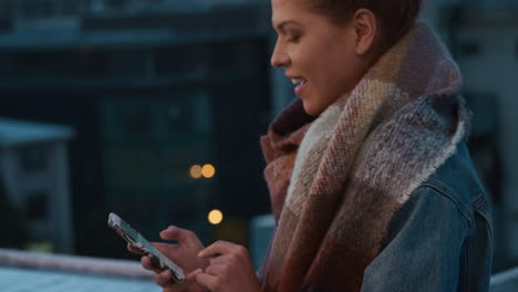 schöne junge frau nutzt smartphone auf dem dach in der nacht, schreibt sms, sendet nachrichten, genießt mobile kommunikation, surft in sozialen medien, teilt wochenend-lifestyle