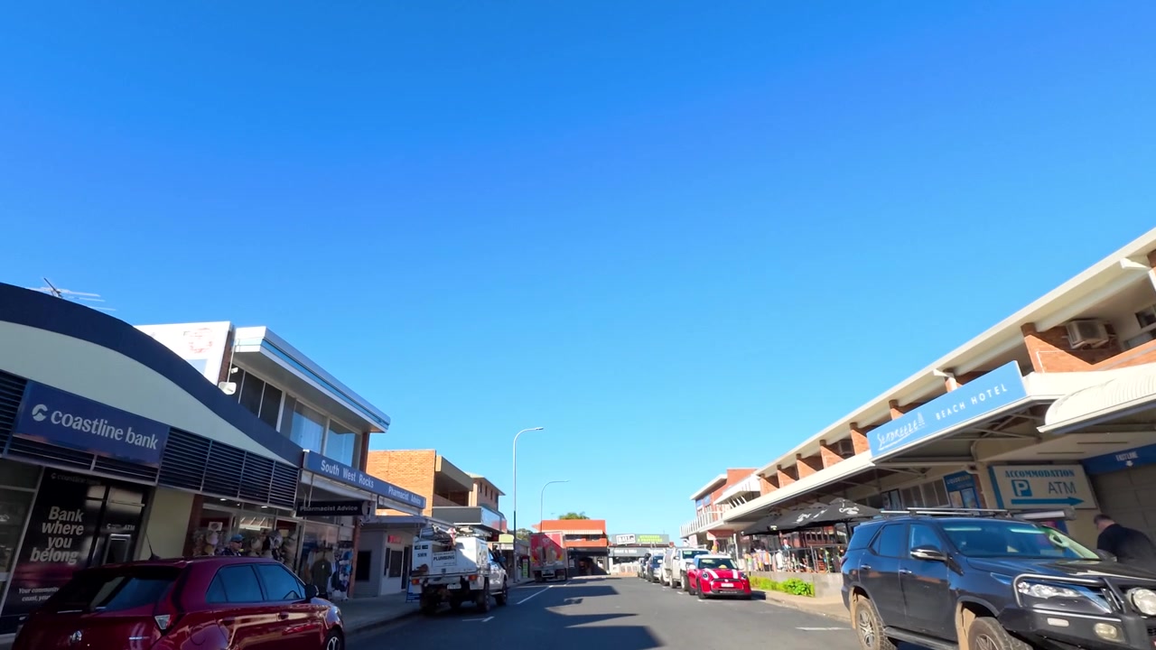 Wide angle tracking shot of commercial storefronts and parked vehicles in South West Rocks, Australia.