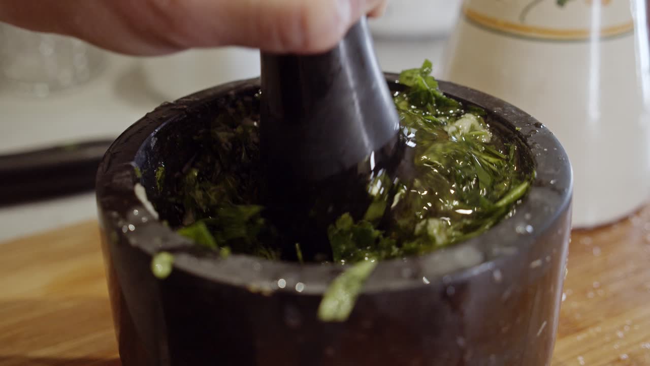 machacar a mano una salsa saludable con hierbas en un tazón negro de cerámica