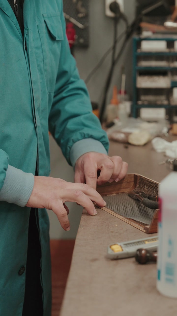 Close up hands applying glue to wooden piece on workbench with tools in workshop vertical