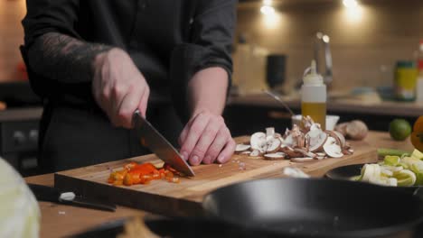 Red-chilis-being-cut-on-a-wooden-board-by-professional-chef-in-an-elegant-black-shirt-with-tattoos