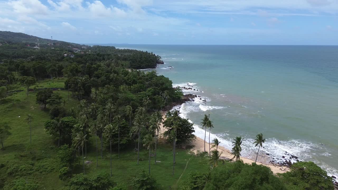 Scenic aerial footage of Koh Lanta, Thailand, showing a remote tropical coastline with lush palm trees, crystal clear turquoise water, rocky shore and hidden beaches in the distance
