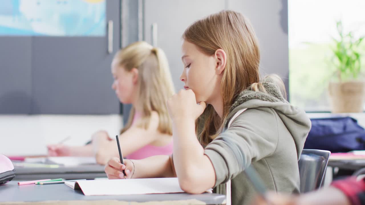 Diverse schoolchildren writing and sitting at desks in school classroom