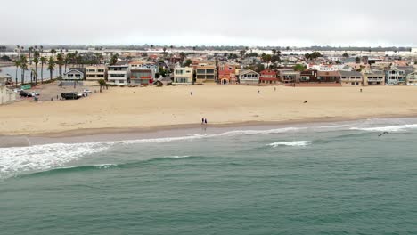 Aerial-sideways-view-of-Silver-Strand-beach,-bathing-area-waterfront-houses-on-Cloudy-day