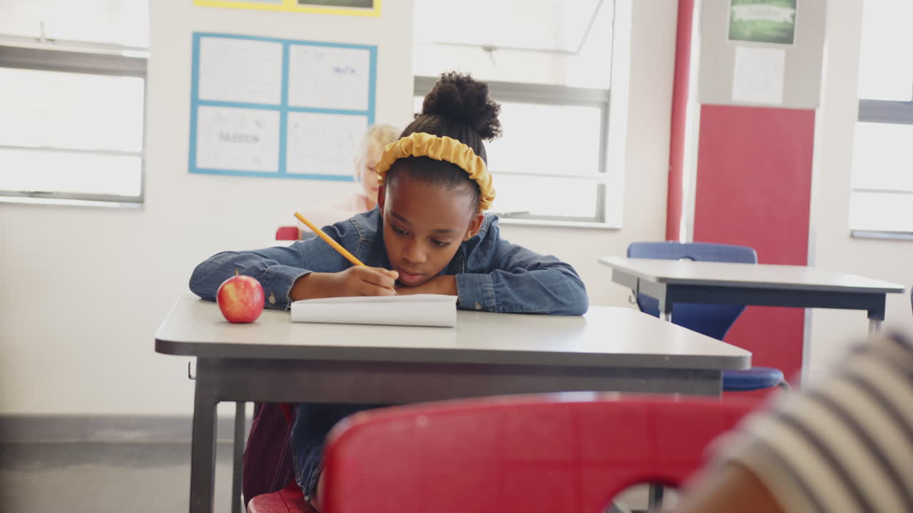 In school, girl writing in notepad at desk with apple, focusing on work