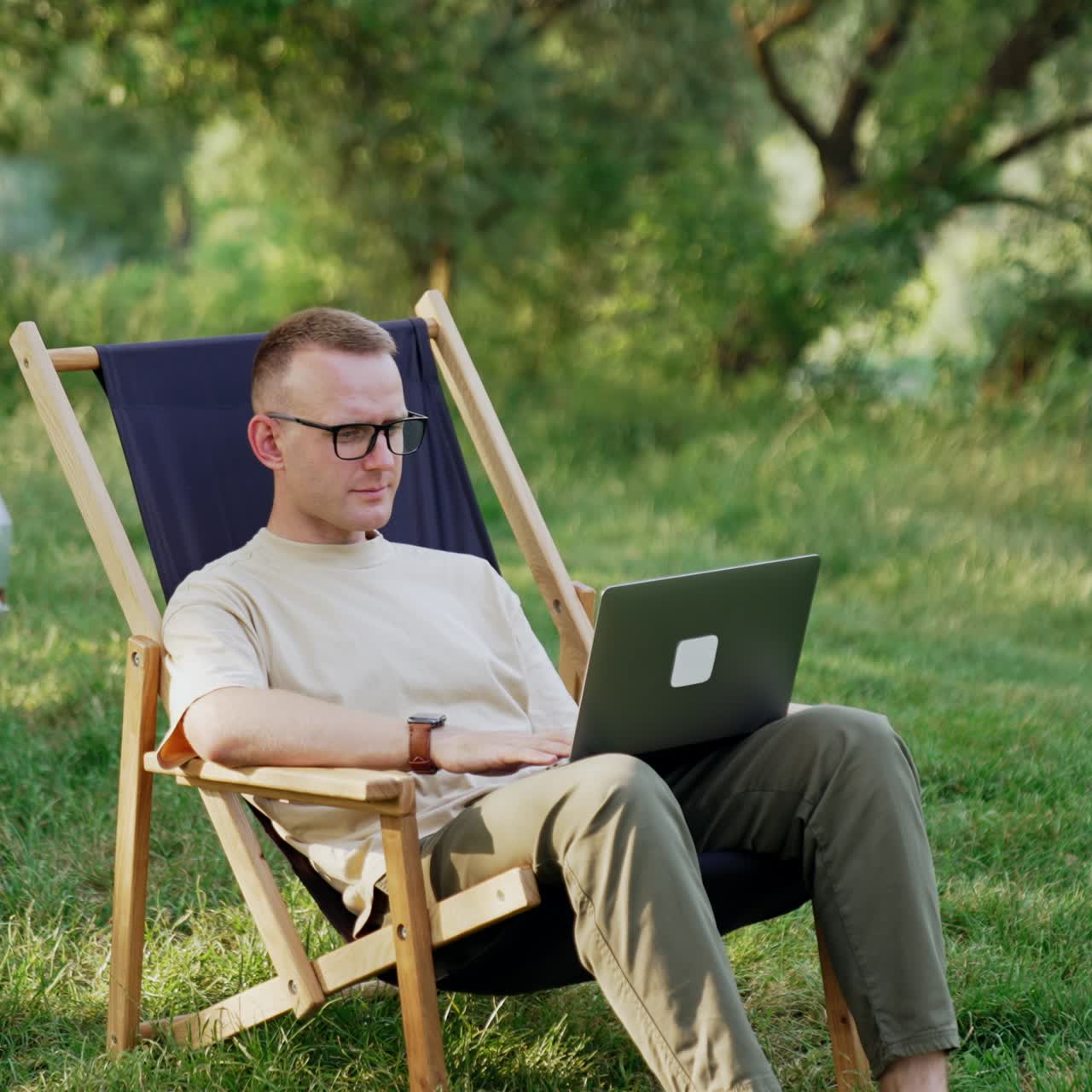 Caucasian freelancer starting work on laptop. Man opens laptop sitting in chair on the meadow. Car at backdrop