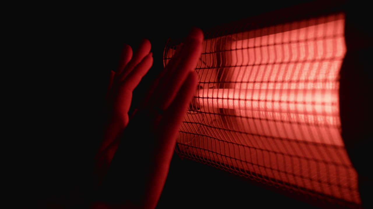 Hands warming near a heater in the dark
