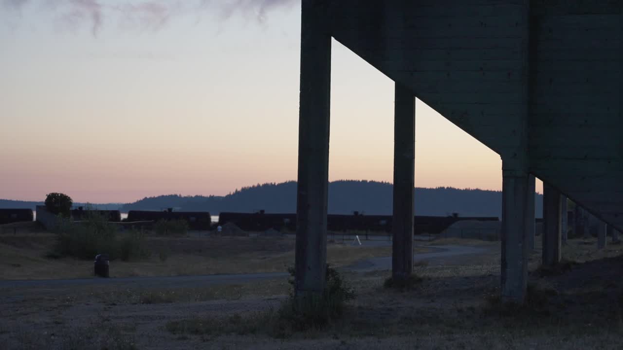Treno che passa al tramonto dietro una struttura con montagne.