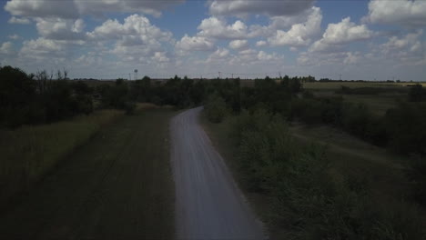 Dusty-road-in-the-countryside-with-cloudy-sky-and-blue,-seen-cars-passing