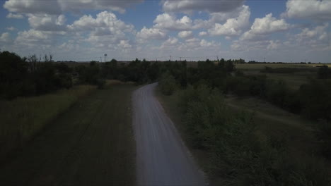 dusty road in the countryside with cloudy sky and blue, seen cars passing