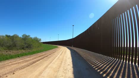 Pov-Conduciendo-En-La-Vía-De-Servicio-Entre-Una-Zanja-Y-El-Muro-Fronterizo-Entre-Estados-Unidos-Y-México