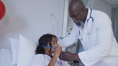 Afroamerikanischer-Männlicher-Arzt,-Der-Einem-Gemischtrassigen-Mädchen,-Das-Im-Krankenhausbett-Liegt,-Ein-Sauerstoffmaskenbeatmungsgerät-Anlegt