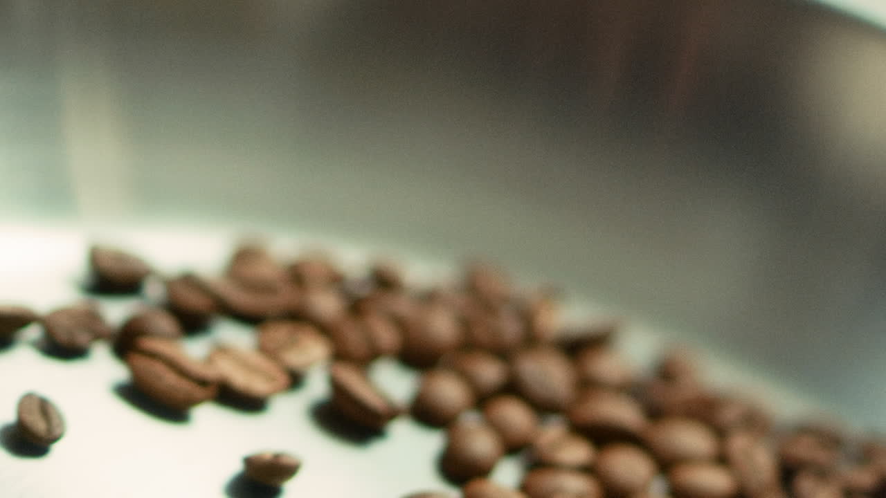 Macro of coffee beans tossing on metal pan in slow motion. Roasted coffee seeds