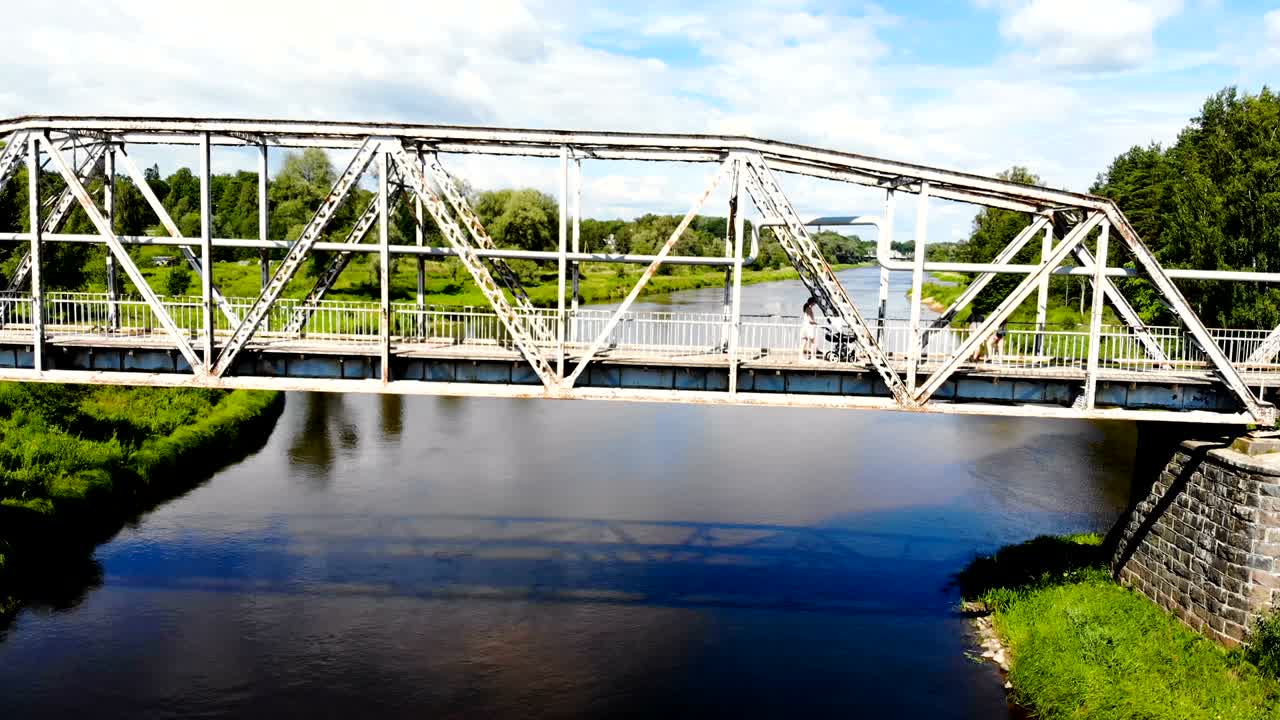 아름다운 강을 가로지르는 금속 다리의 드론 영상. 어머니가 아기 바가로 걸어가고 있습니다.