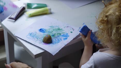 toddler painting with potatoes and blue ink on her table