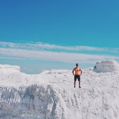 sporty man with muscular body on the top of white hill under blue sky. handsome sportsman on beautiful summer landscape in the mountains. motion down.