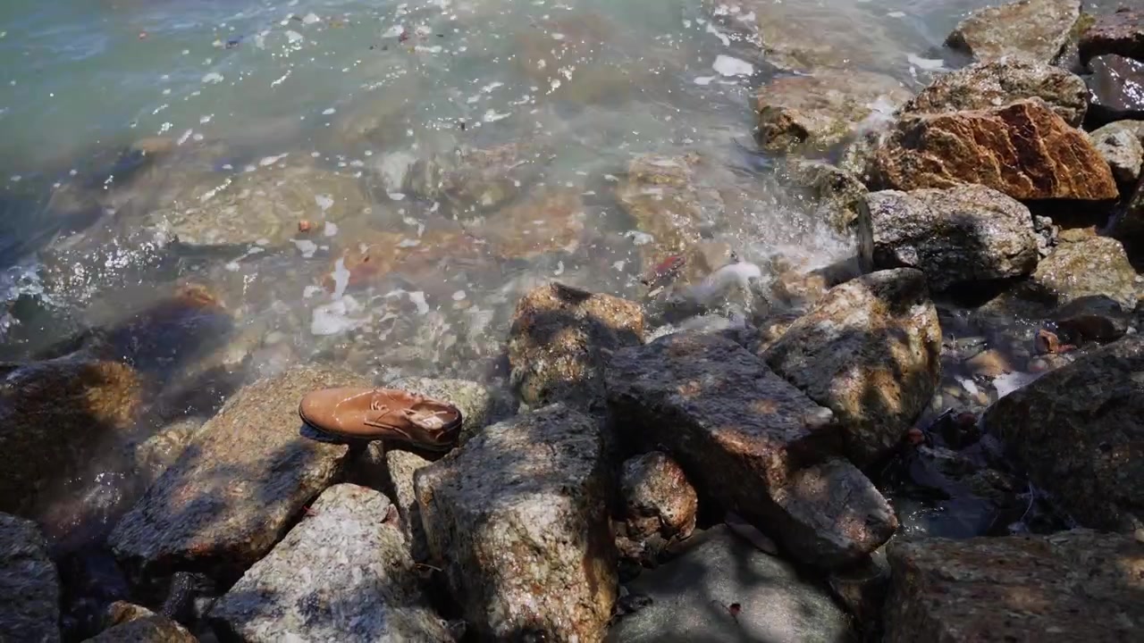 Onde oceaniche lavano una scarpa abbandonata tra le rocce lungo la costa, creando un concetto visivo per detriti marini, inquinamento idrico, rifiuti e conservazione ambientale