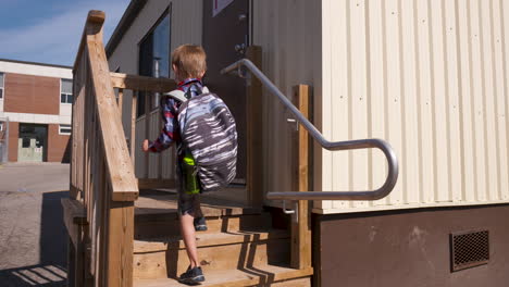 student in a face mask walks up the steps to a portable classroom