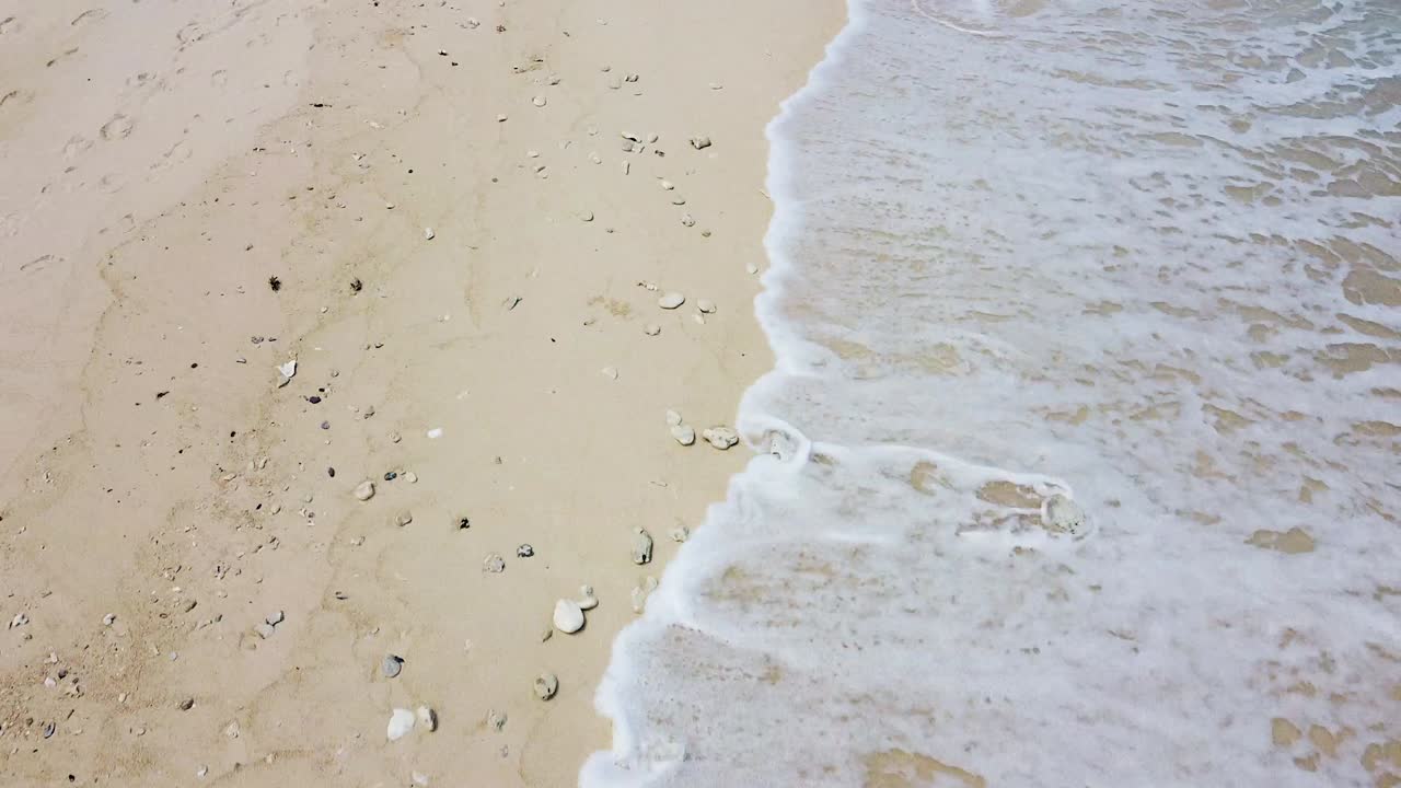 Aerial drone flying close to sandy beach with waves rolling in on remote tropical island of Jaco Island, Timor-Leste, Southeast Asia