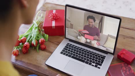 Fröhlicher-Afroamerikanischer-Mann,-Der-Ein-Geschenk-öffnet-Und-Einen-Videoanruf-Zum-Valentinstag-Auf-Dem-Laptop-Tätigt