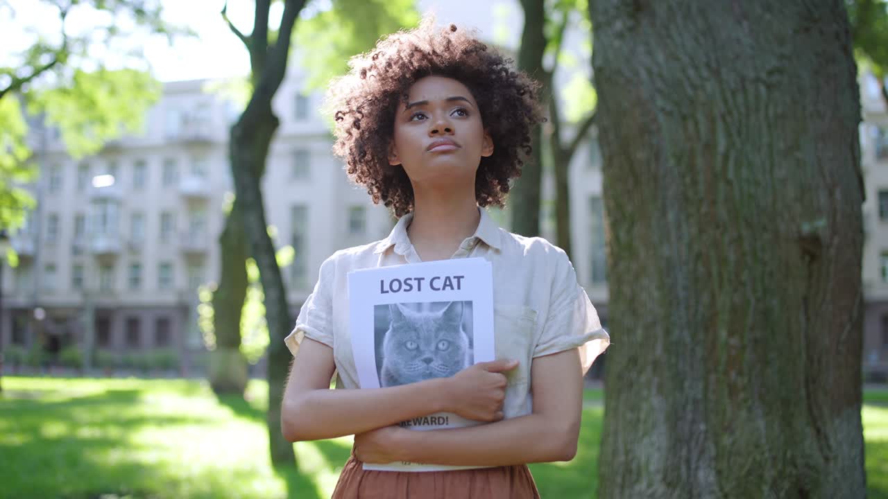 mujer afroamericana molesta mirando a su alrededor, sosteniendo un cartel de gato desaparecido en las manos