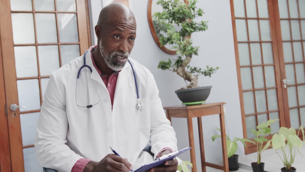 African american male doctor wearing lab coat, holding clipboard and taking notes, slow motion